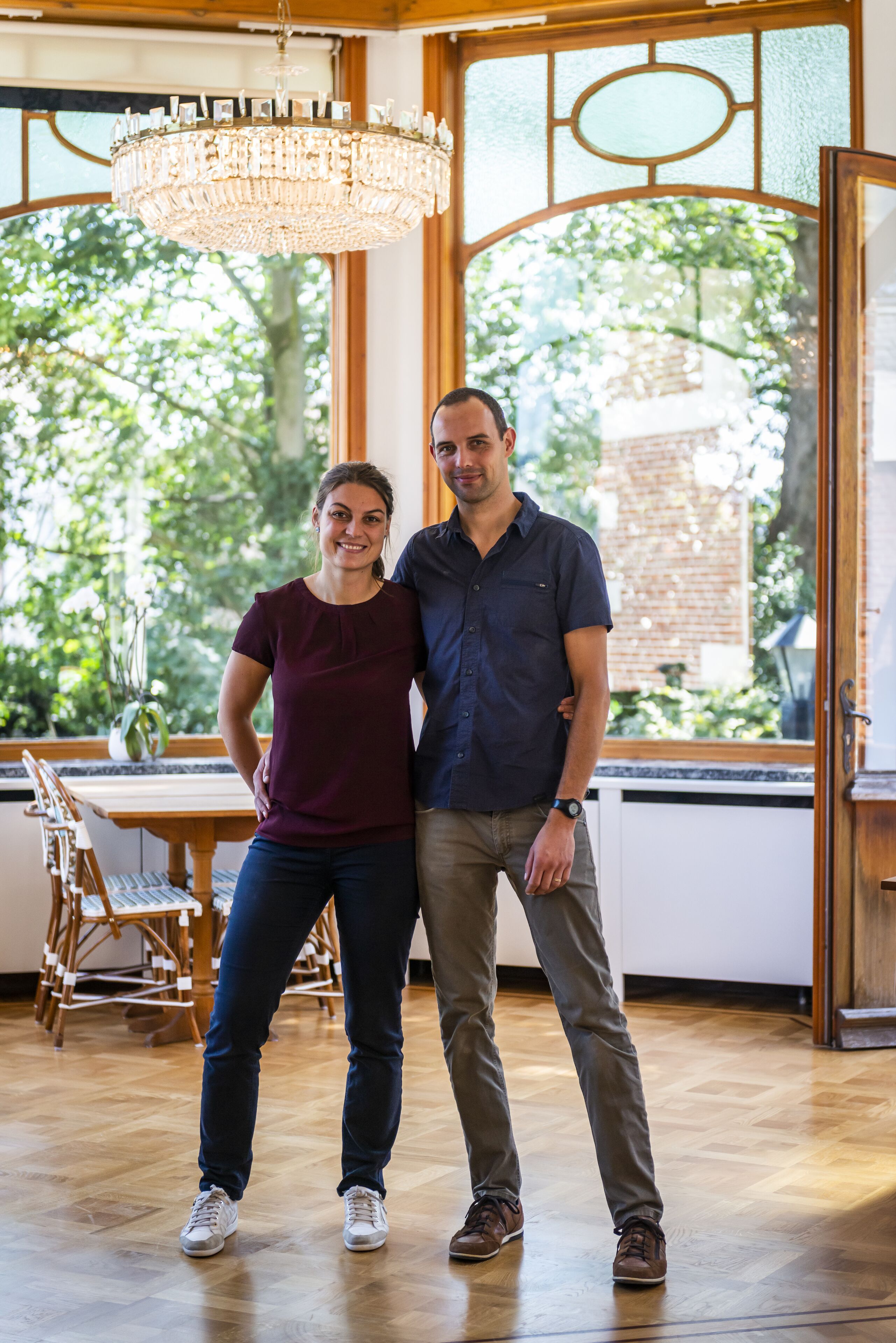 A room with a large window, wooden flooring, and a chandelier.