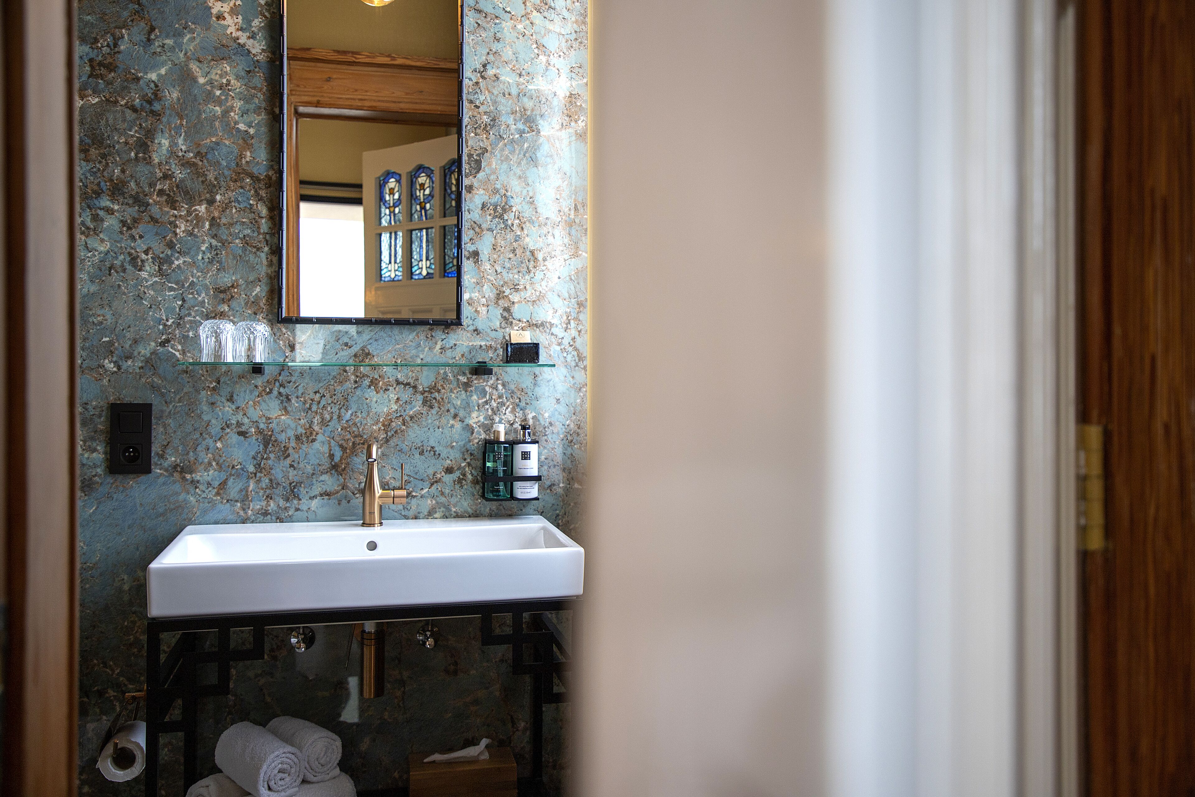 Une salle de bain avec un lavabo blanc, un miroir et un mur en marbre.