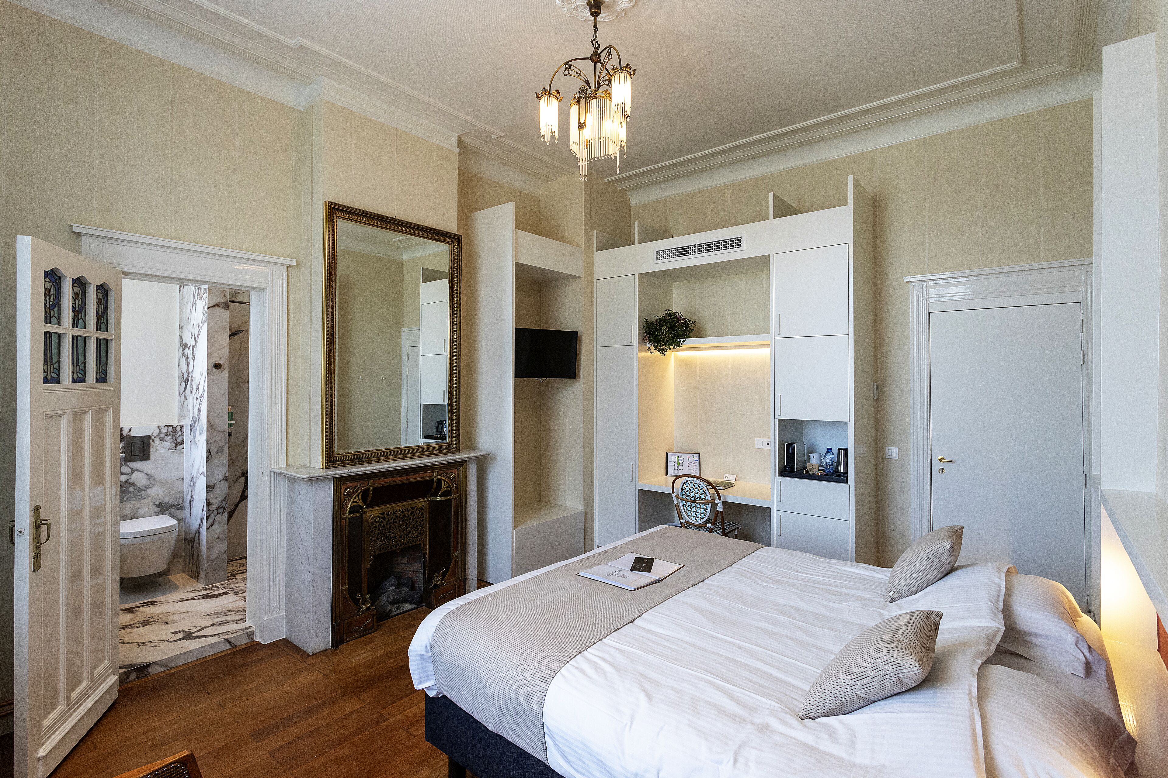 A bedroom with a large bed, a chandelier, a television, and a bathroom visible through an open door.