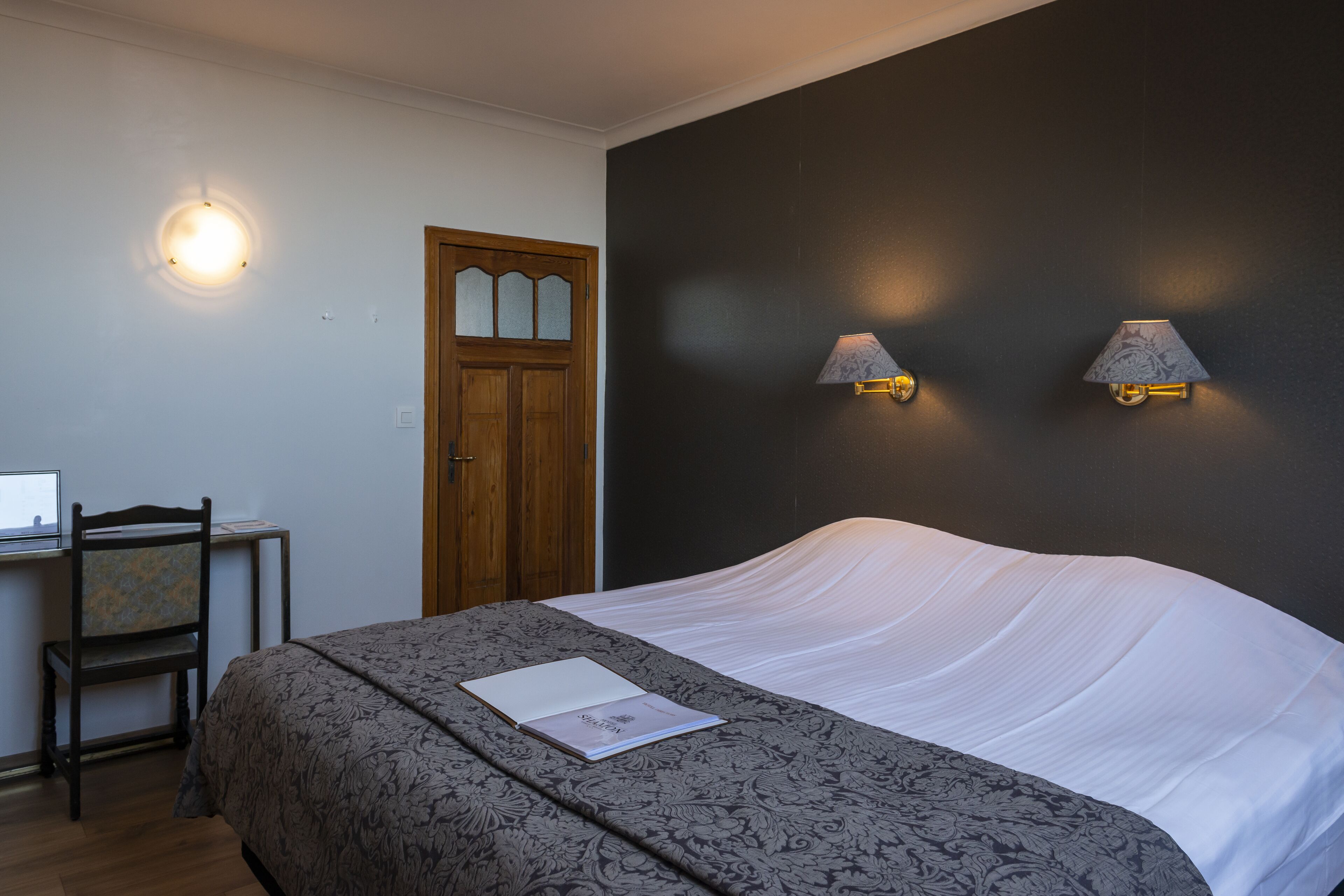 Un dormitorio con una cama, un escritorio y dos lámparas de pared.
