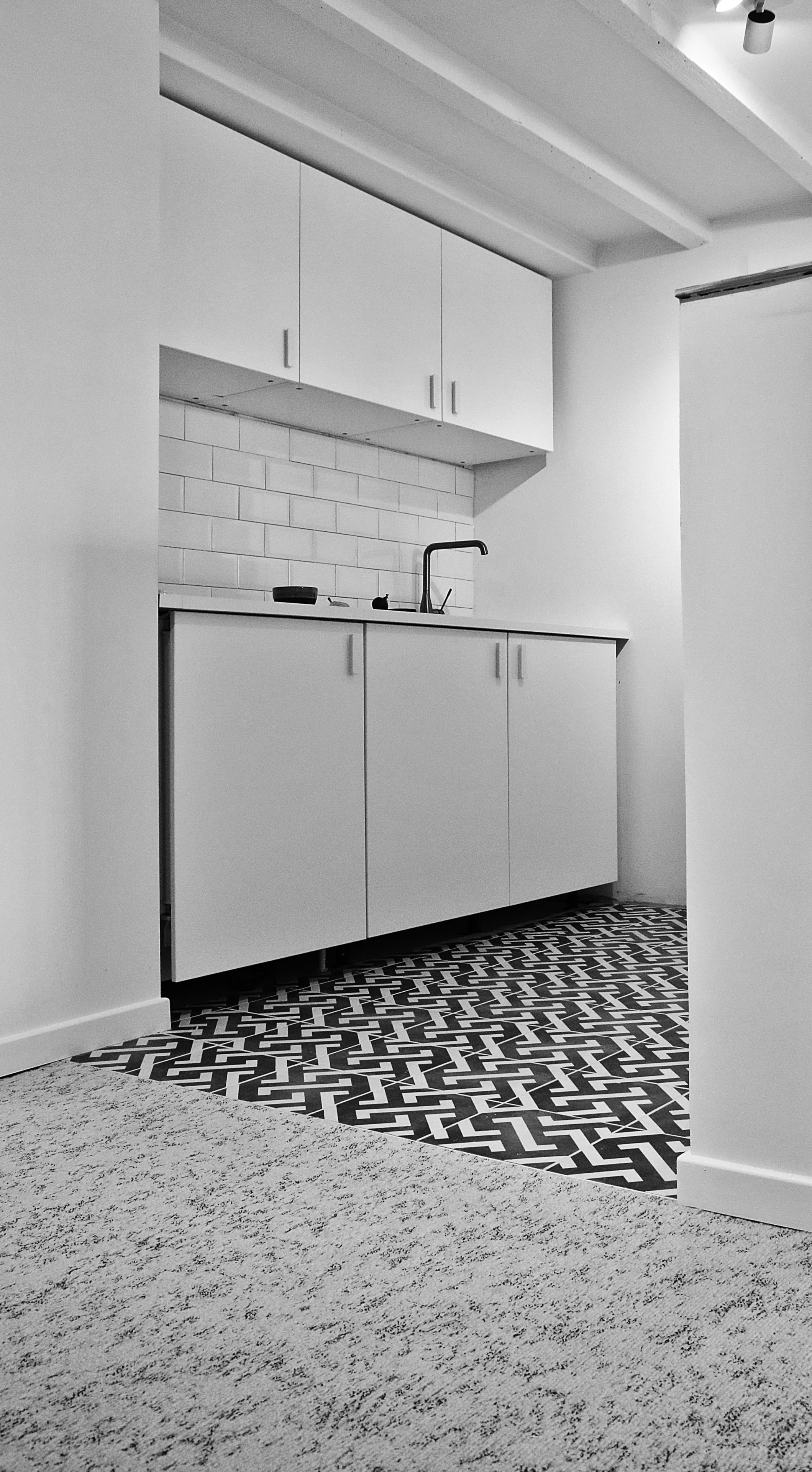 Une cuisine moderne avec des meubles blancs, un pare-feu en carreaux et un sol à motifs.