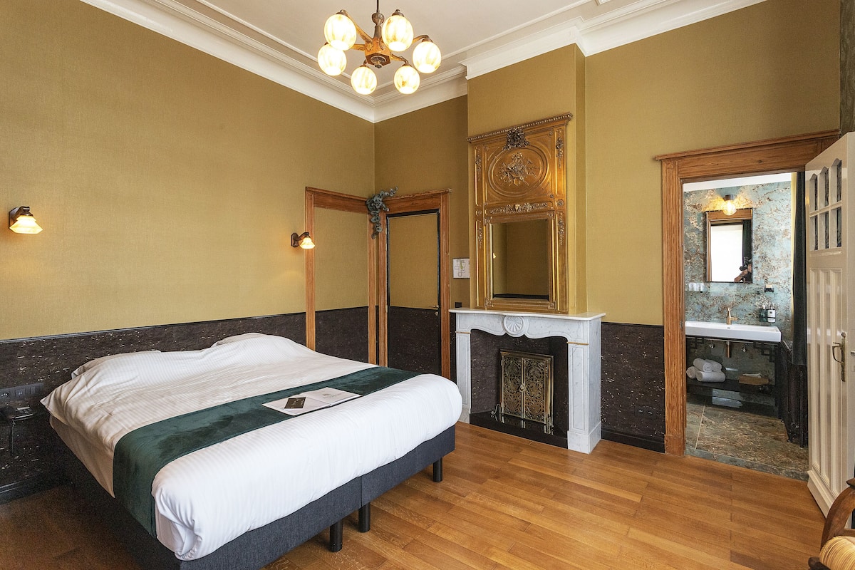Quarto de hotel com uma cama grande, lareira, espelho e porta de madeira.