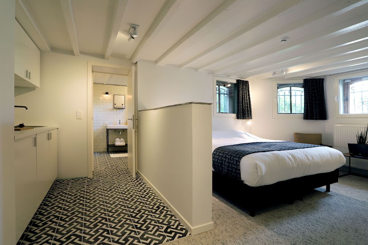 Quarto moderno com uma cama grande, um closet espaçoso, banheiro com parede de azulejos brancos e vista para o exterior pela janela.