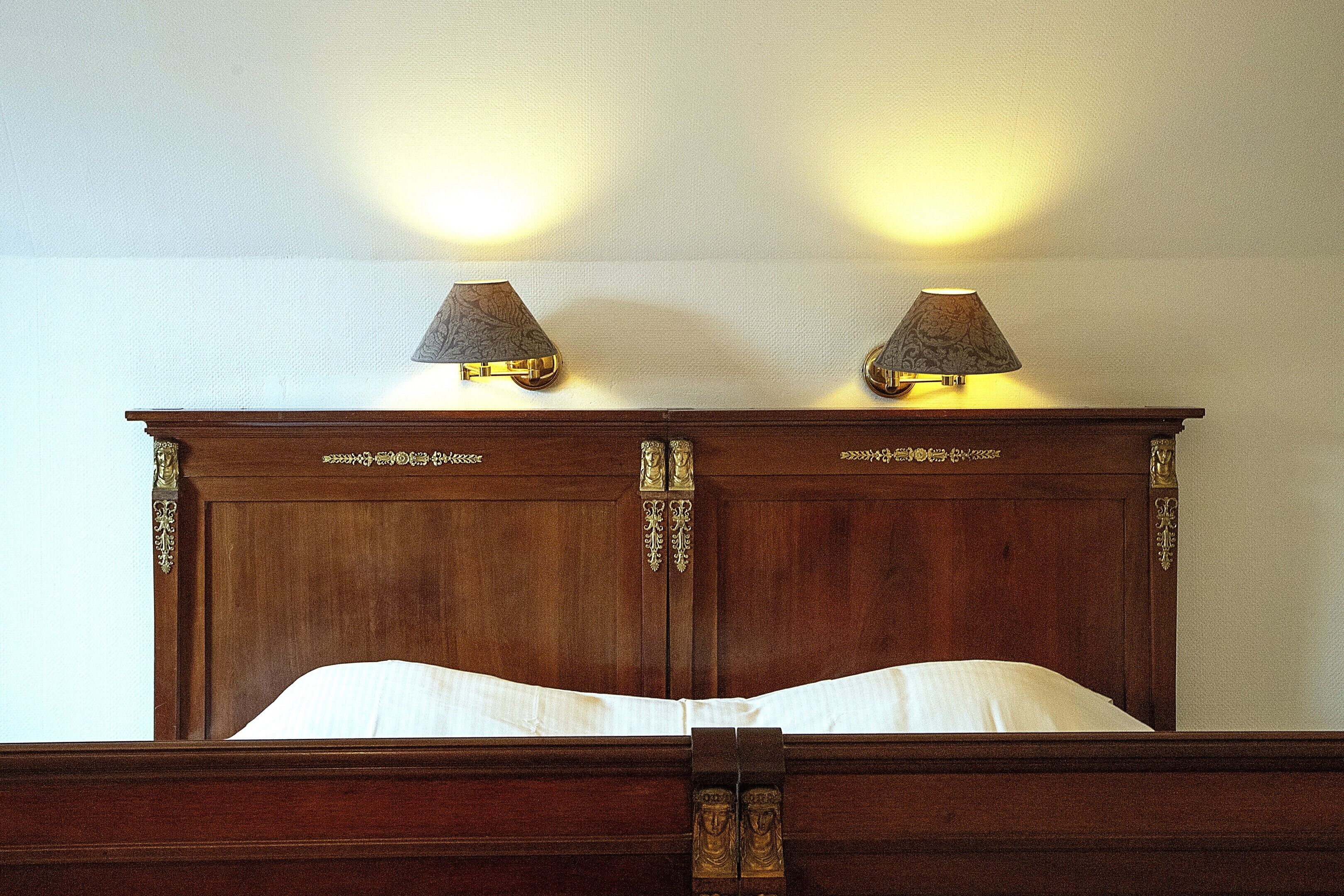 A wooden bed with a headboard featuring decorative carvings and two wall-mounted lamps.