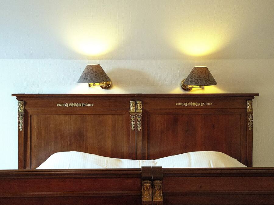 A wooden bed with a headboard featuring decorative carvings and two wall-mounted lamps.