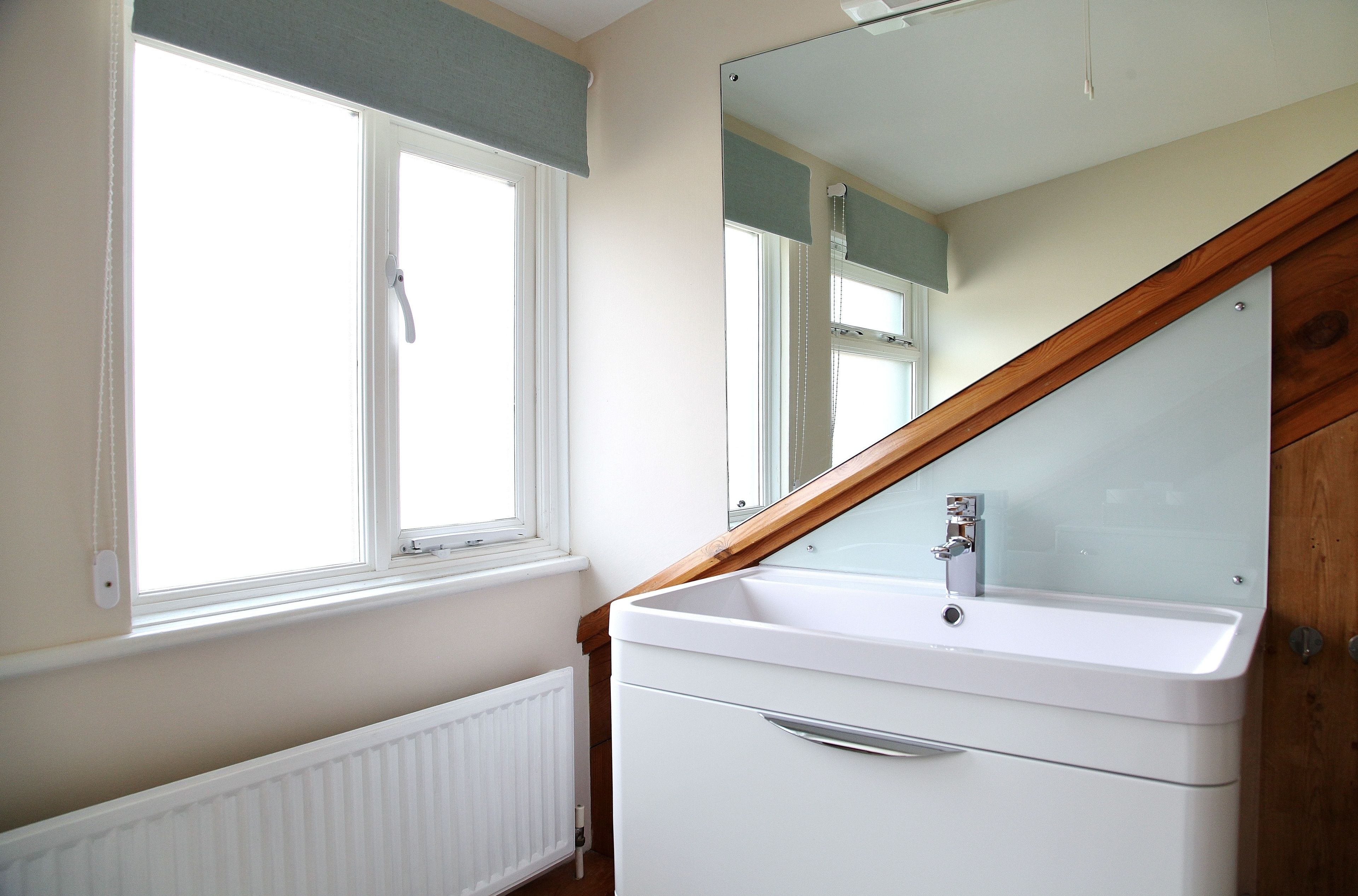 A bathroom with a white sink, a mirror, and a window with a white blind.