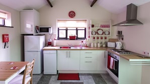A compact kitchen with white cabinets, a microwave, a sink, and a stove. There is a window with a view of the outside, and a red rug on the floor. - Greenbanks Hotel (Dereham)