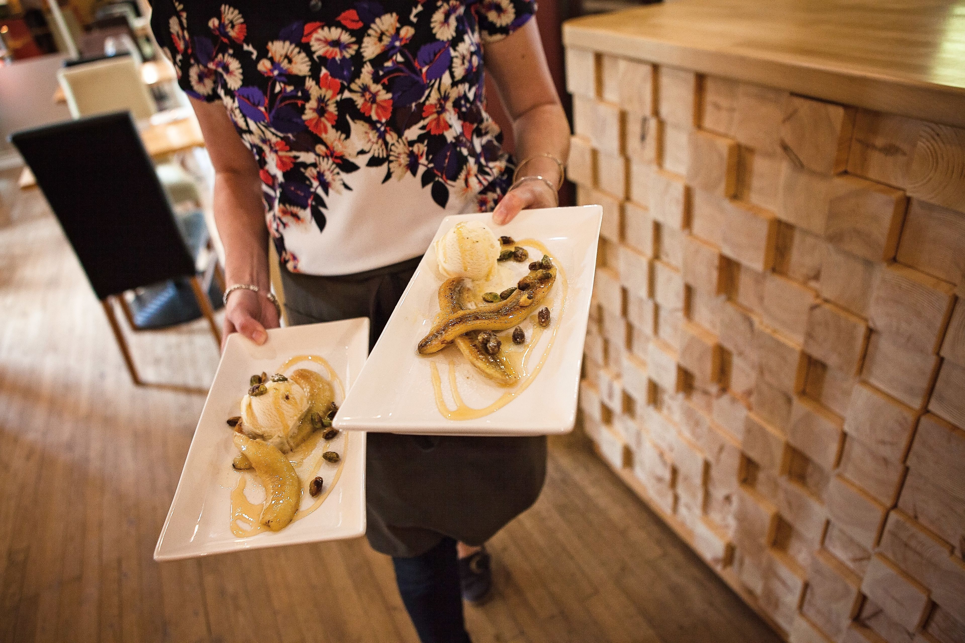A person holding two square plates with desserts, one with a banana and the other with ice cream and nuts.