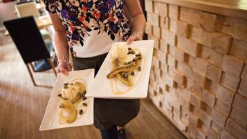 A person holding two square plates with desserts, one with a banana and the other with ice cream and nuts.