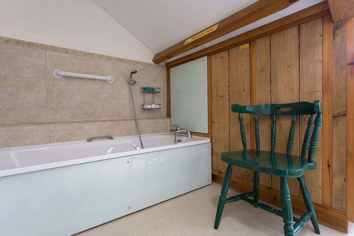 A bathroom with a bathtub, a wooden chair, and a wooden wall.