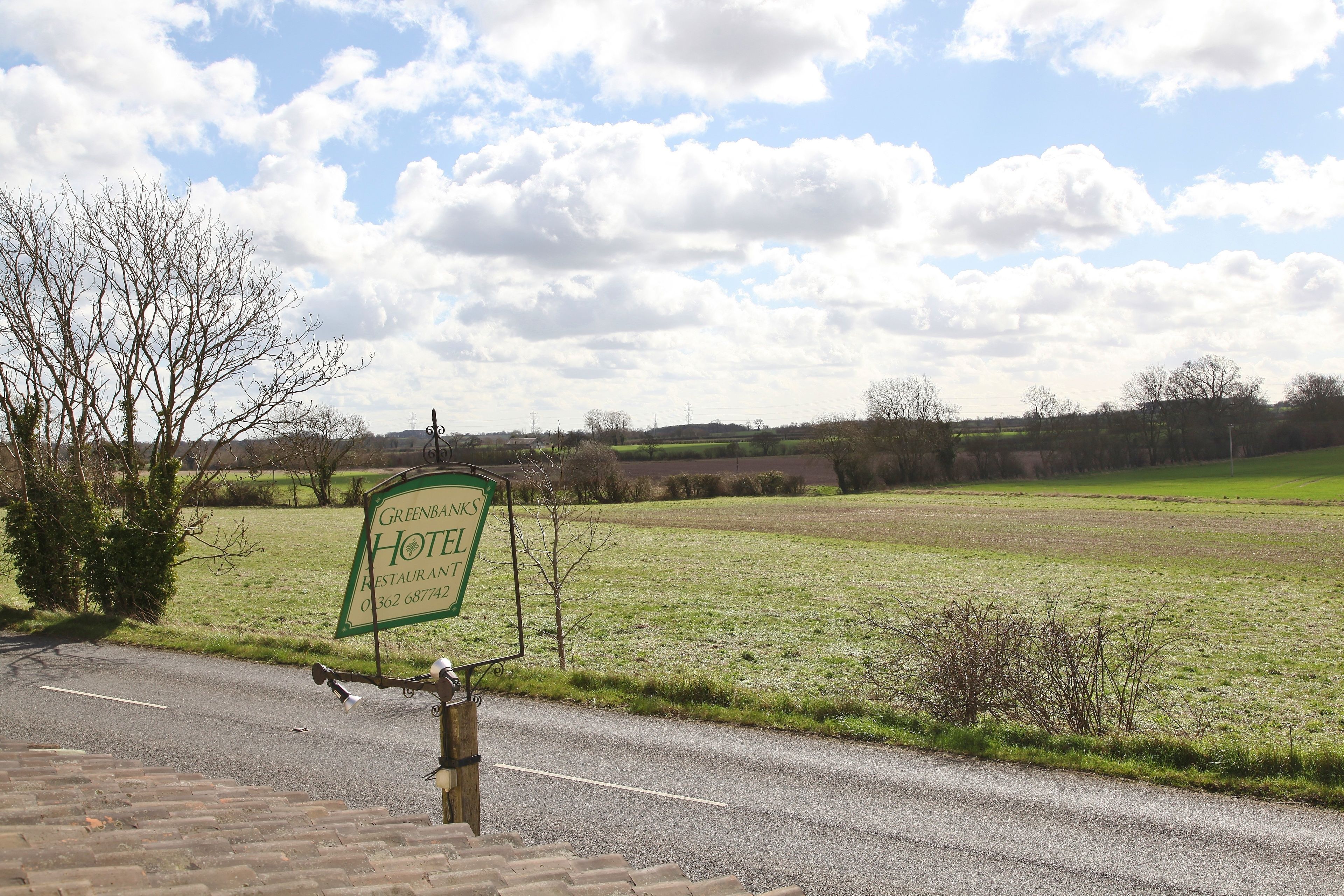 A sign for Green's Hotel Restaurant and a rural landscape with fields and trees.
