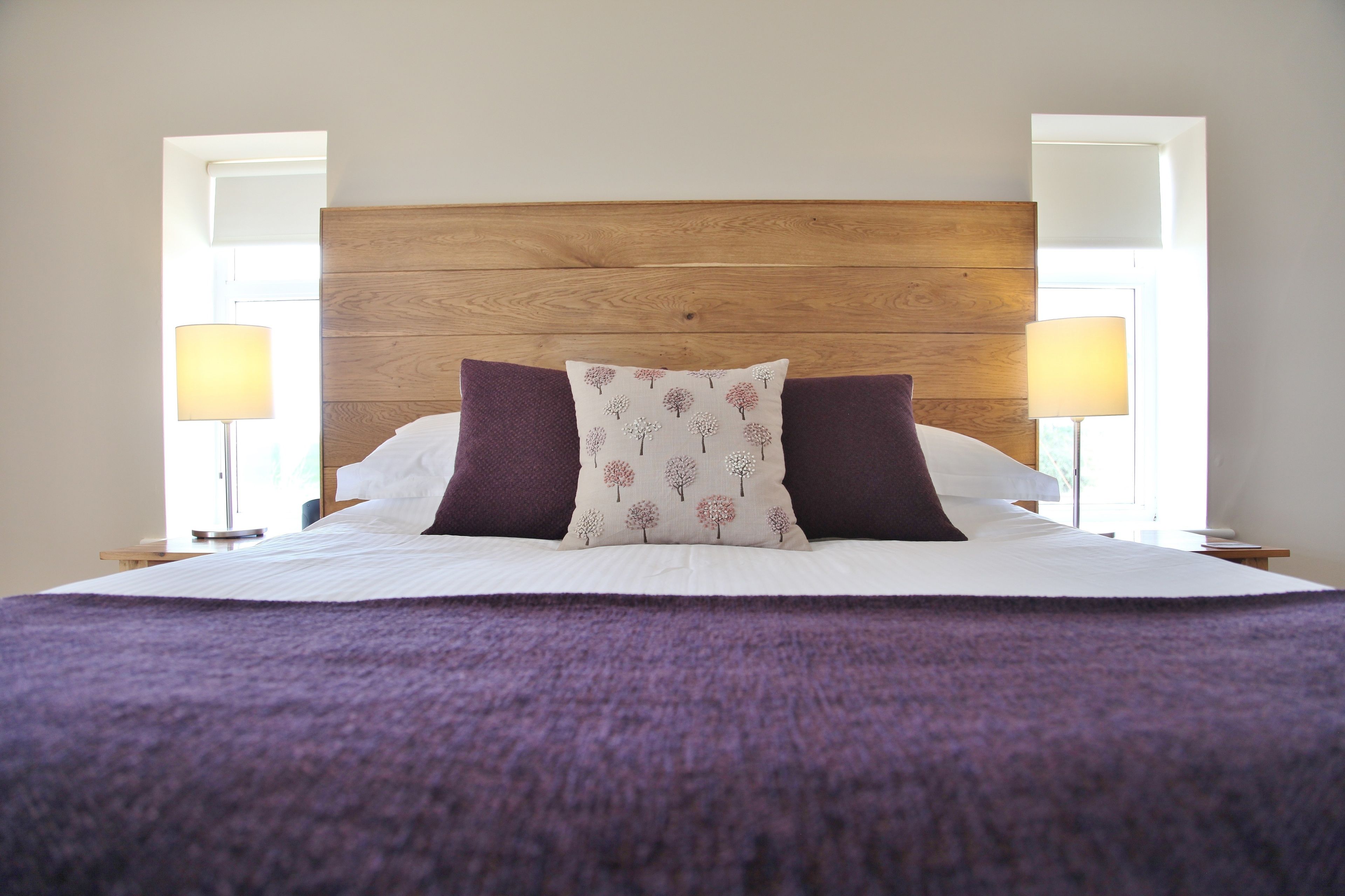 A neatly made bed with a wooden headboard, two pillows, and a purple blanket.