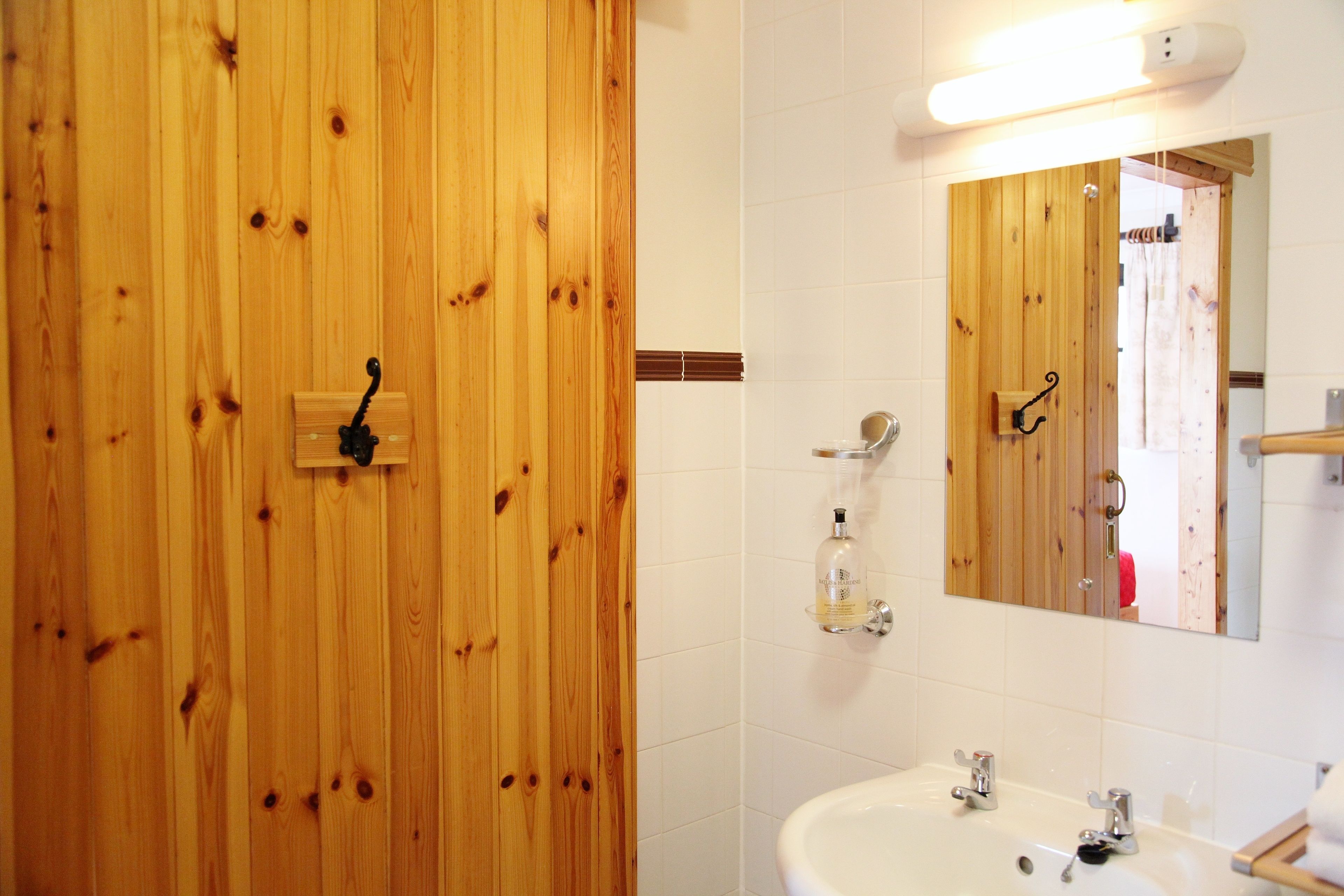 A wooden door with a towel rack, a white tiled wall, a mirror, and a sink with faucets.