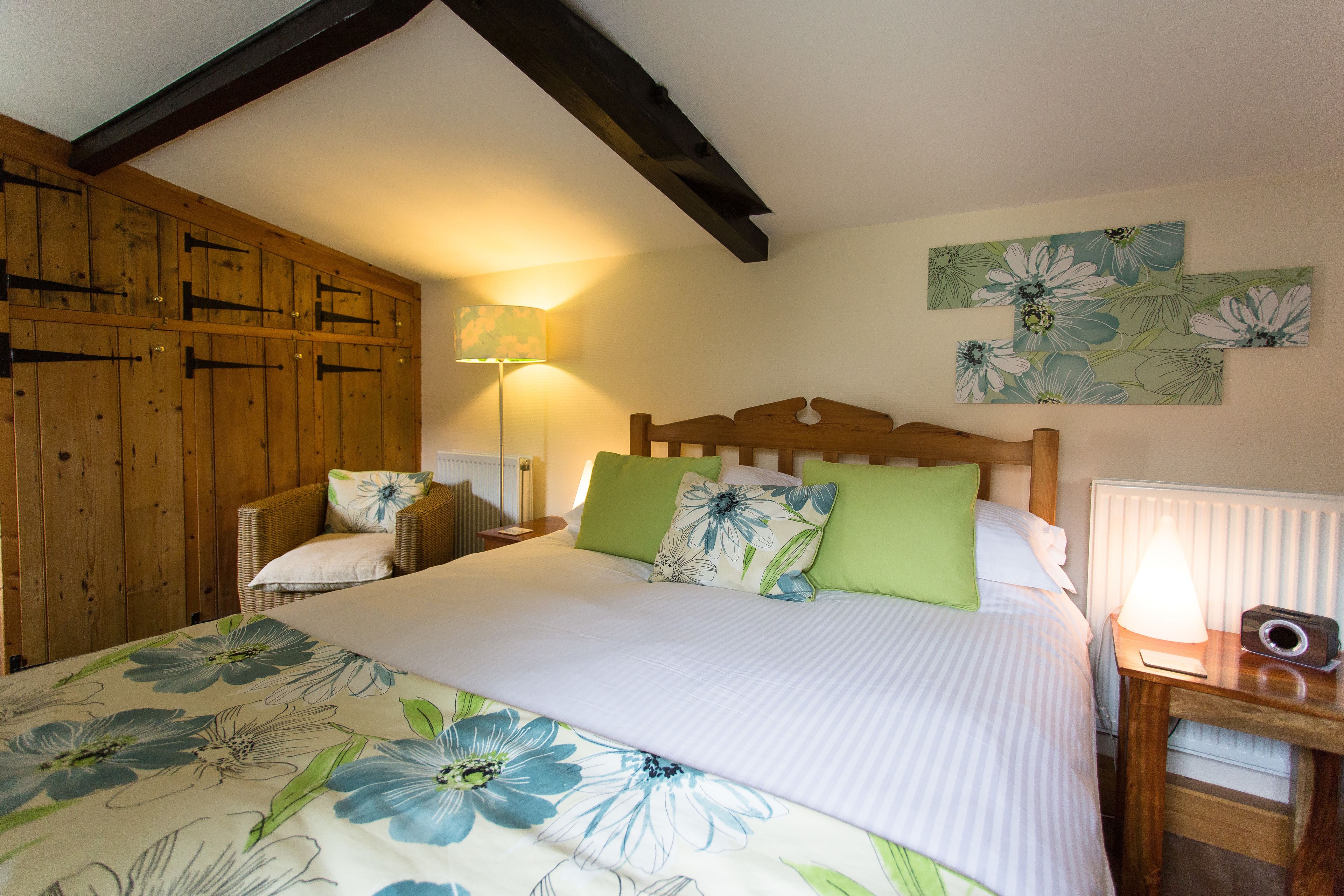 A bedroom with a large bed, wooden headboard, green and white pillows, a nightstand with a lamp, and wooden paneling on the walls.