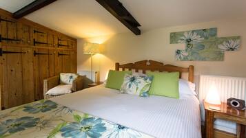 A bedroom with a large bed, wooden headboard, green and white pillows, a nightstand with a lamp, and wooden paneling on the walls.