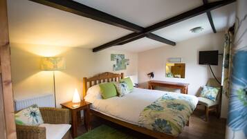 A bedroom with a wooden bed, two chairs, a bedside table, a lamp, and artwork on the walls.