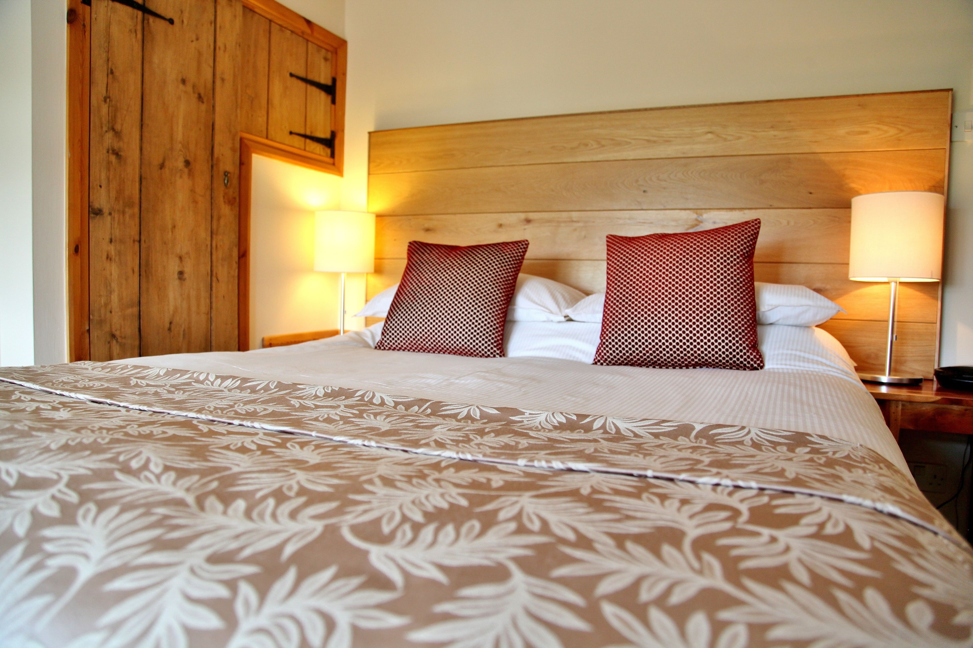Un letto rifatto con cura, una coperta a motivi, due cuscini decorativi e due abat-jour.