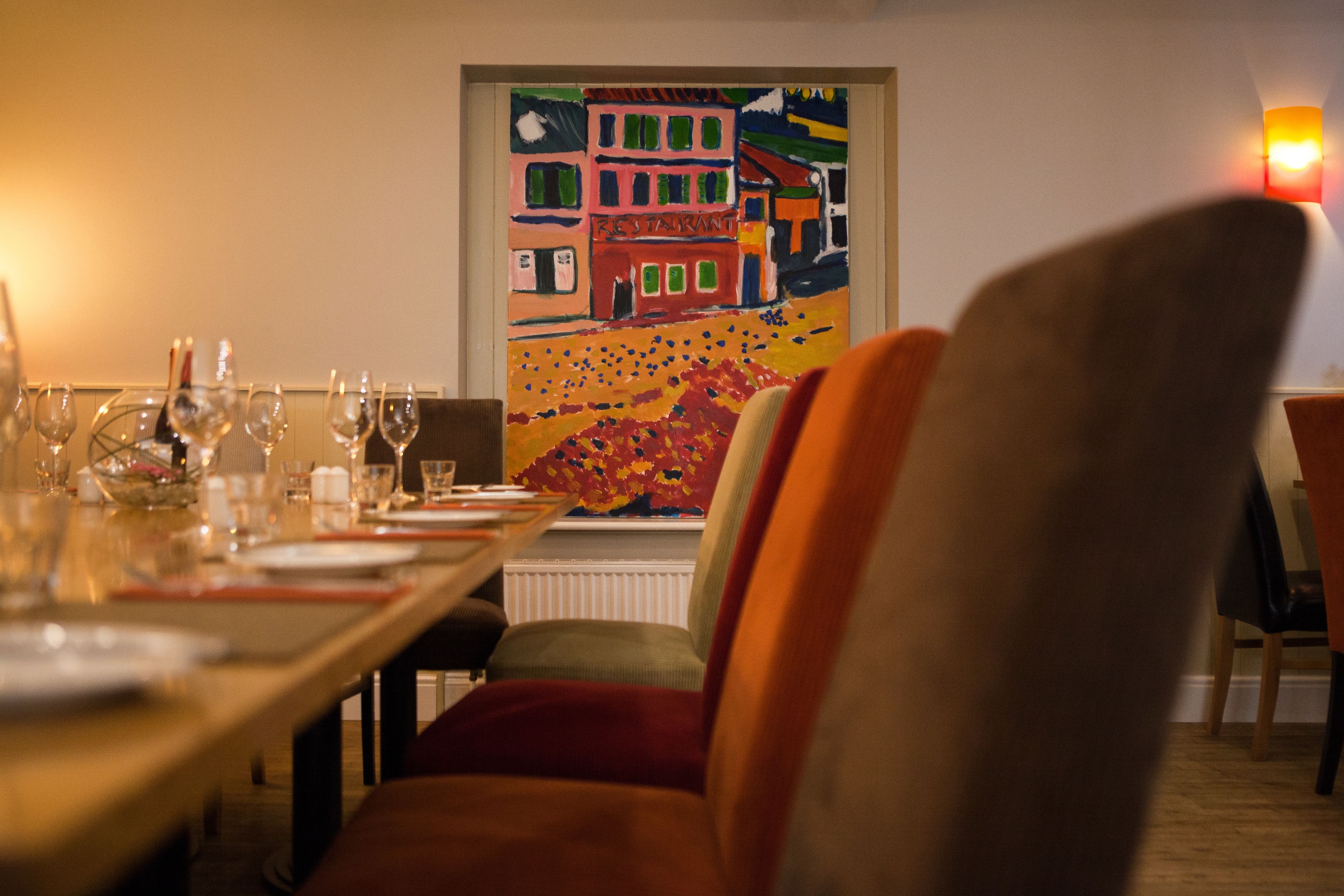 A dining area with a table set for a meal, a colorful painting on the wall, and a chair in the foreground.