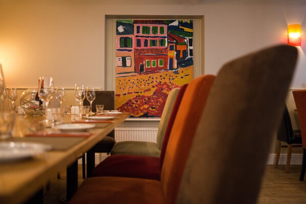 Un comedor con una mesa dispuesta para una comida, un cuadro colorido en la pared y una silla en primer plano.