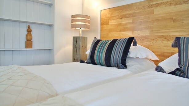 A neatly made bed with striped pillows, a wooden headboard, and a wall-mounted shelf with a decorative item. - Greenbanks Hotel (Dereham)
