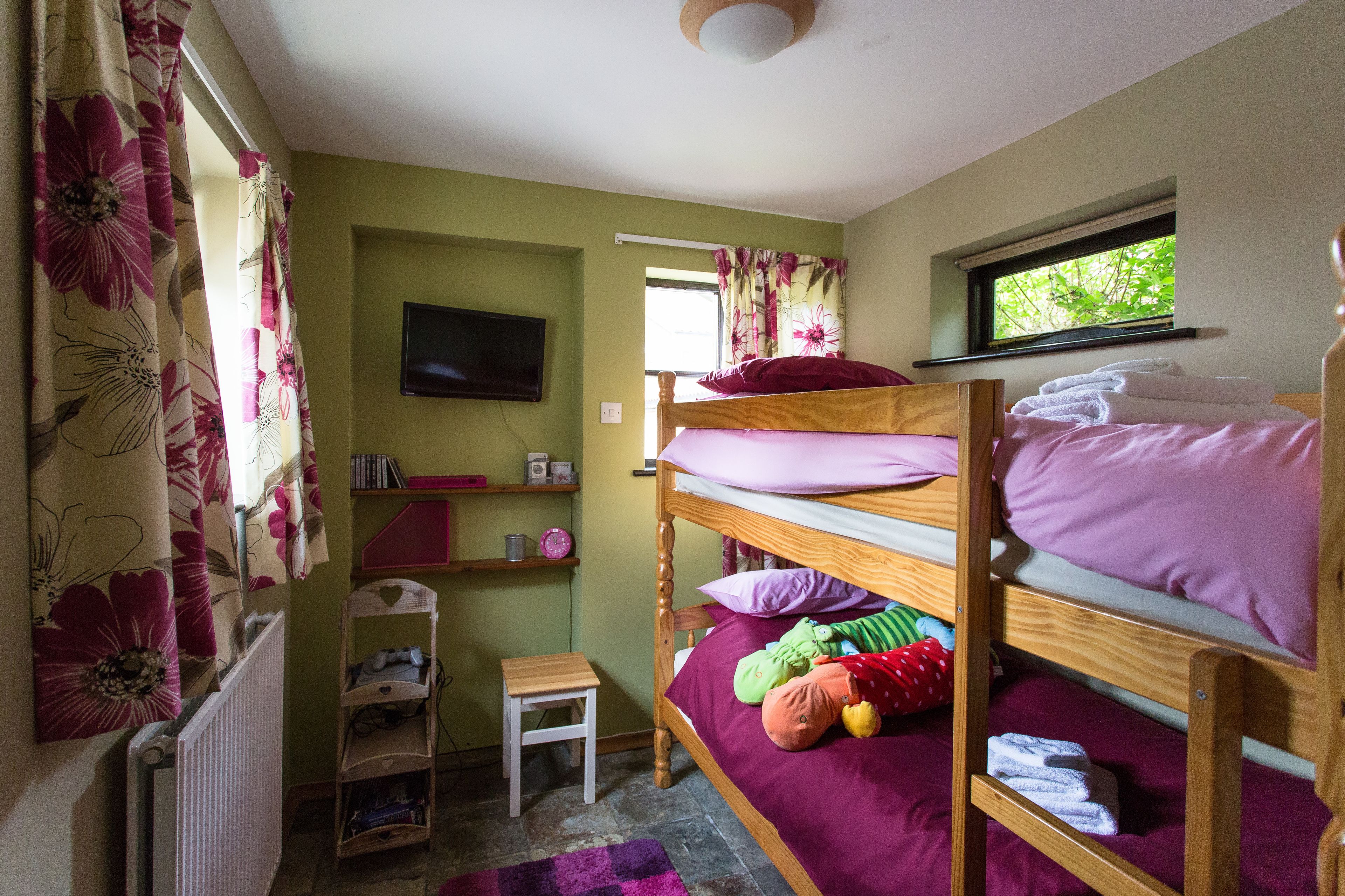A bunk bed room with a television, a window with curtains, a radiator, and a small table.