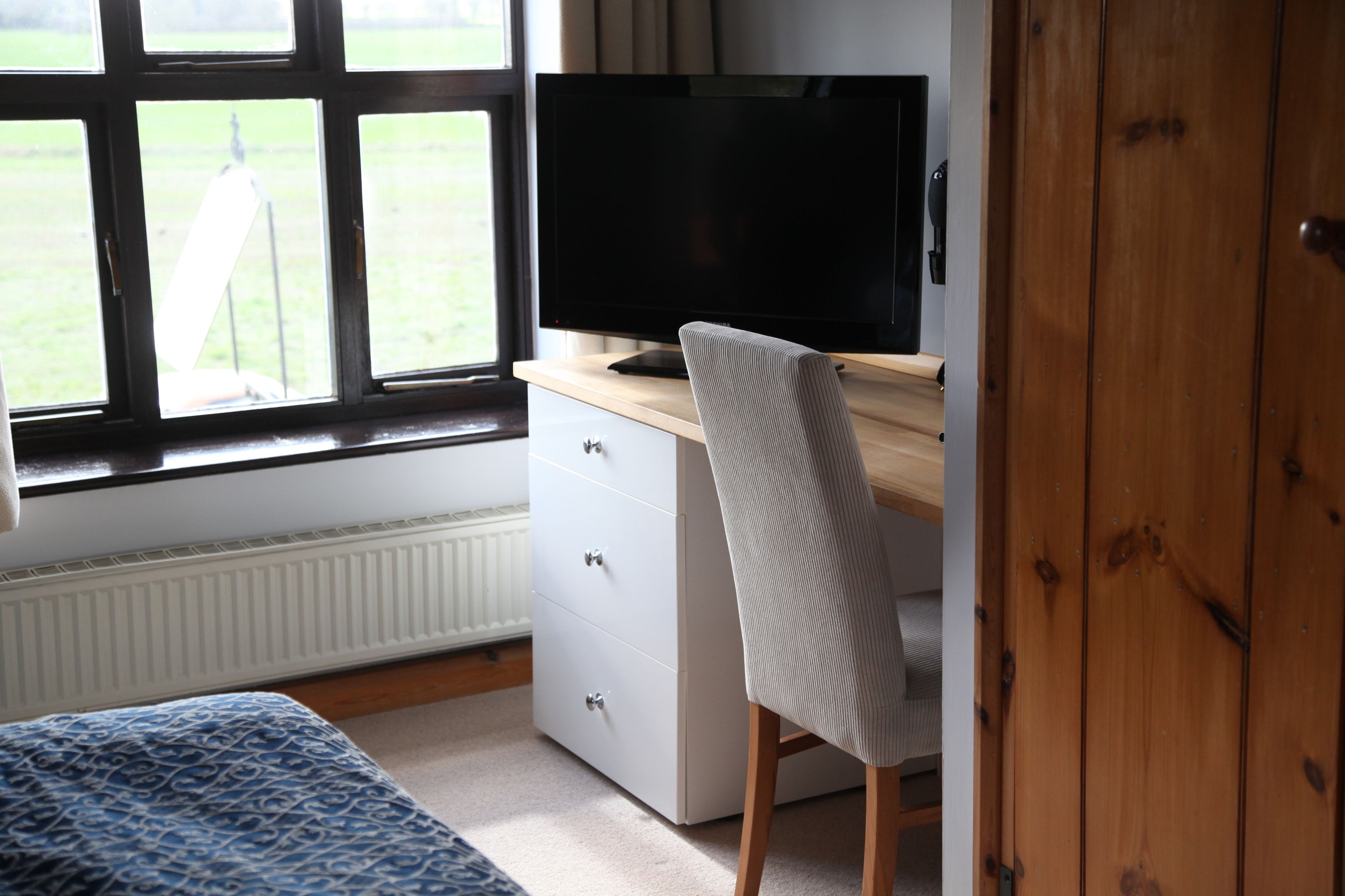 A bedroom with a bed, a desk with a computer, a window, and a door.