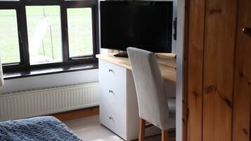 A bedroom with a bed, a desk with a computer, a window, and a door.