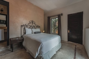 A bedroom with a bed, a nightstand, a lamp, a window with curtains, and a door.