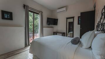 A bedroom with a bed, a television, a door, and a window with curtains.