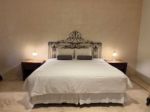 A neatly made bed with a decorative headboard, two bedside lamps, and a simple nightstand. - Art 64 Guest House – Adults Only (Mérida)