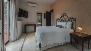 Quarto com cama, mesa de cabeceira, luminária, televisão fixada na parede e janela com cortinas.