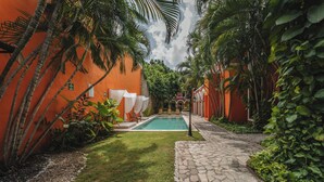 Uma área de piscina com um caminho de pedra, cercada por vegetação exuberante e paredes alaranjadas.