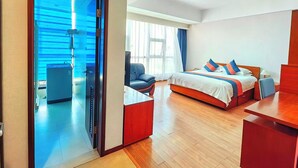 Quarto de hotel moderno com uma cama, escrivaninha, cadeira, mesinha de centro e banheiro com chuveiro.