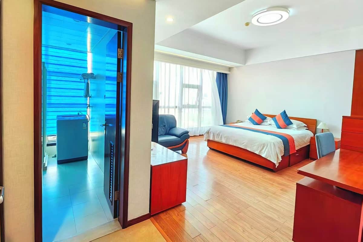 Habitación de hotel moderna con cama, escritorio, silla, mesita y baño con ducha.