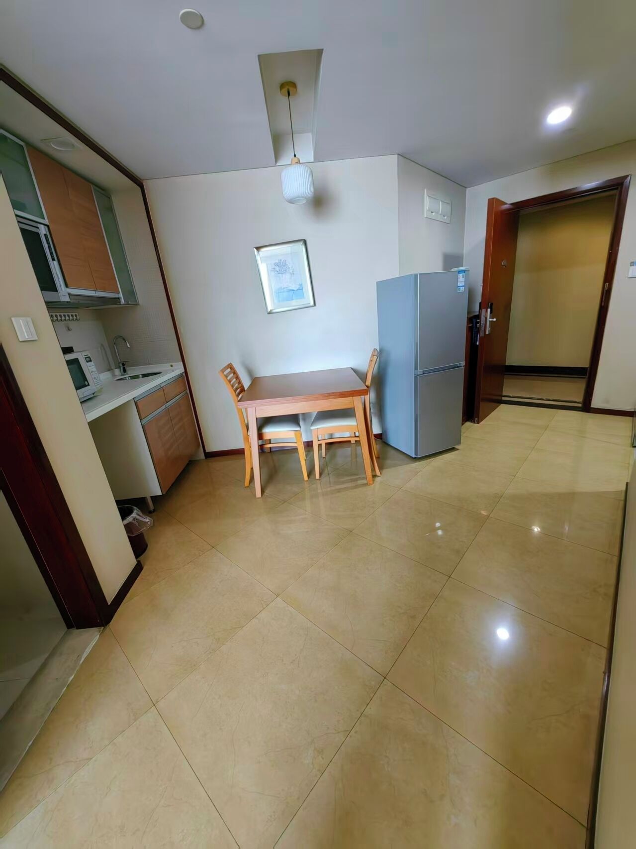 A compact kitchen with a dining table and chairs, a refrigerator, and a microwave.