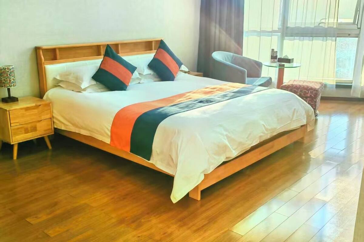 Una habitación de hotel moderna con una cama de madera, una mesita de noche, una silla y una pequeña mesa.