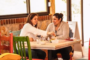 Two people sitting at a table with a brick wall behind them, a window to the left, and a signboard to the right. - El Remanso de Tecpan (Tecpan Guatemala)