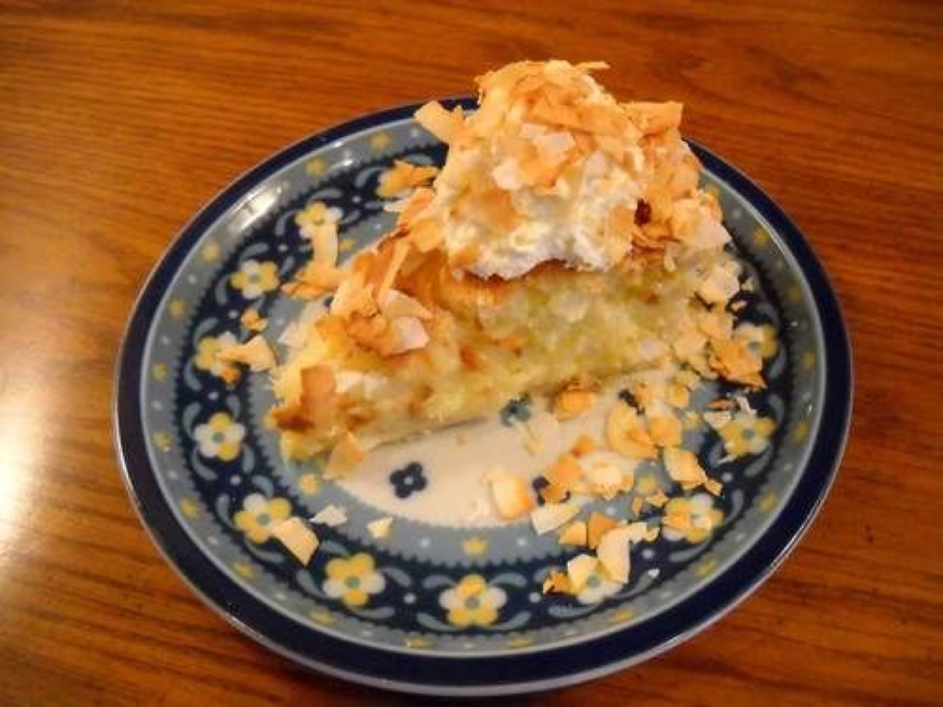 Une part de gâteau parsemée de copeaux de noix de coco, présentée sur une assiette à motifs floraux.