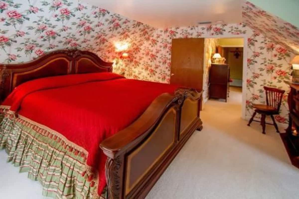 A bedroom with a wooden bed, floral wallpaper, and a red bedspread.