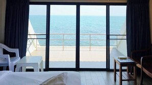 Habitación de hotel con cama, una pequeña mesa, una silla y vista al mar a través de amplios ventanales.