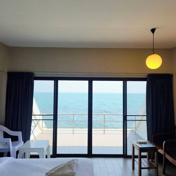 Una habitació d'hotel amb un llit, una taula petita, una cadira i vista al mar a través de grans finestres.