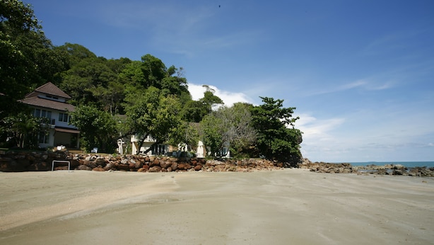 A beach with a house and trees in the background.