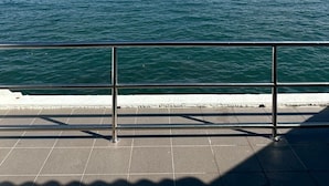 Vista del océano desde una terraza con baldosas y barandilla de metal.