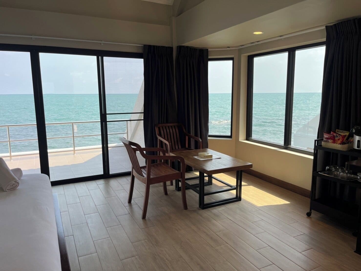 A hotel room with a balcony, a dining table, chairs, a bed, and a shelf with snacks.