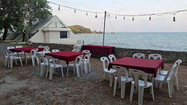 An outdoor dining area with tables and chairs, a small building, and a view of the sea. - Wangkaew Resort (Klaeng)