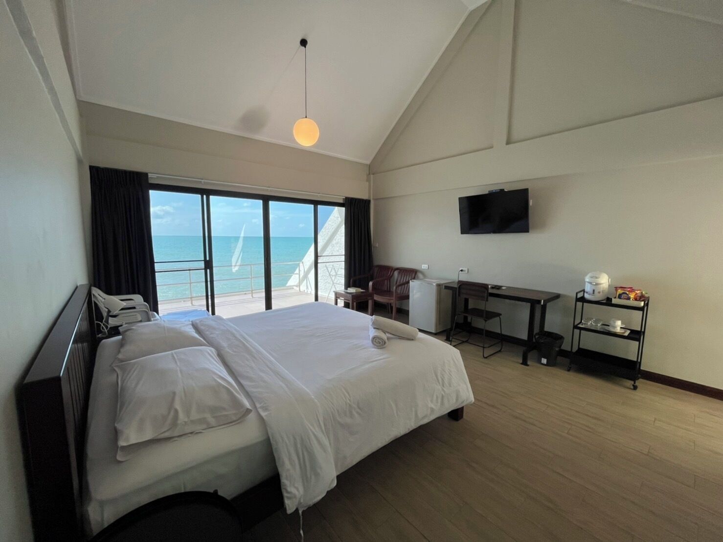 A hotel room with a large bed, a desk, a television, and a view of the sea.