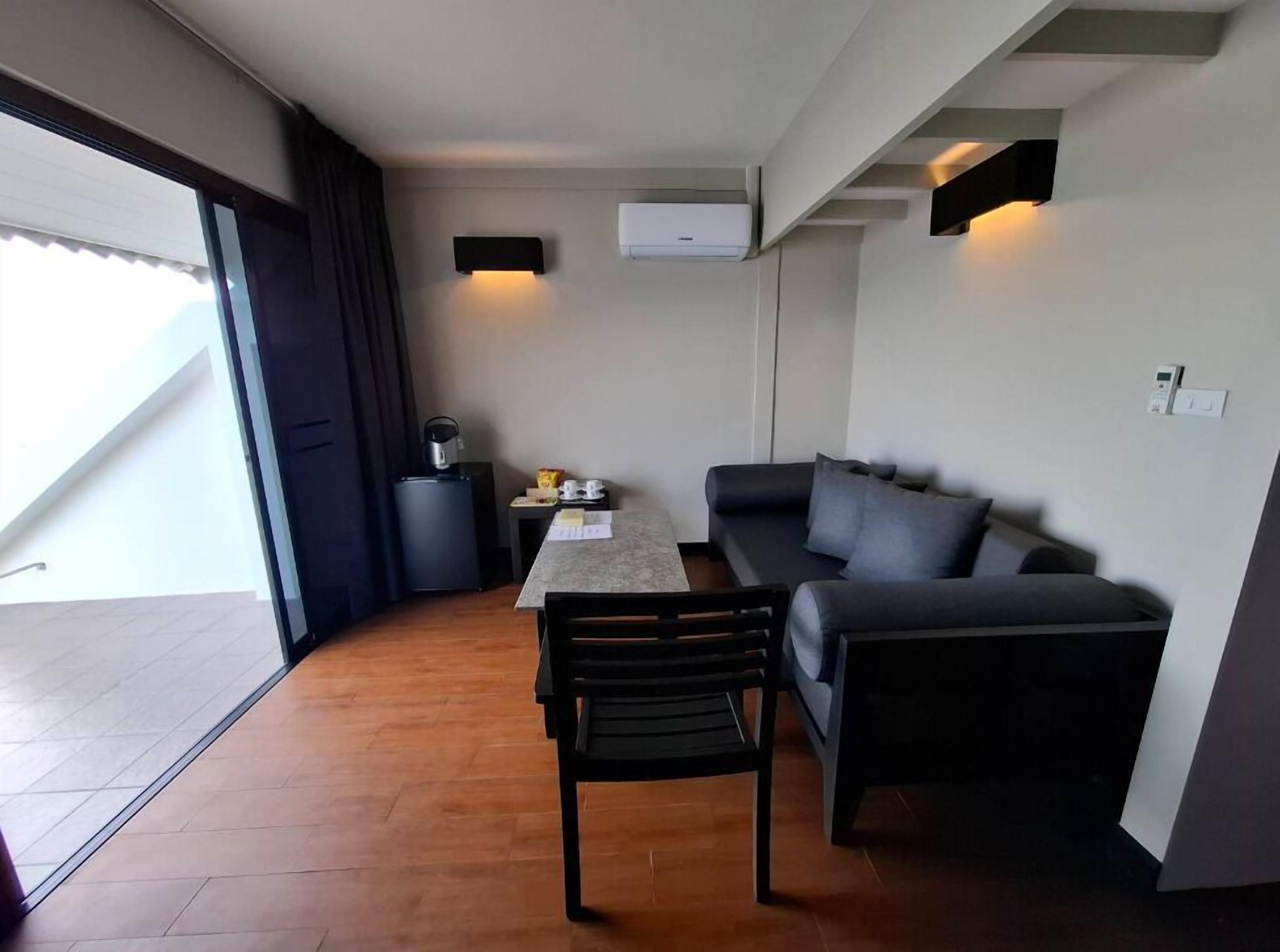 Un espacio habitable compacto con sofá, mesa de comedor y una silla. Hay una puerta corredera que da a un área exterior.