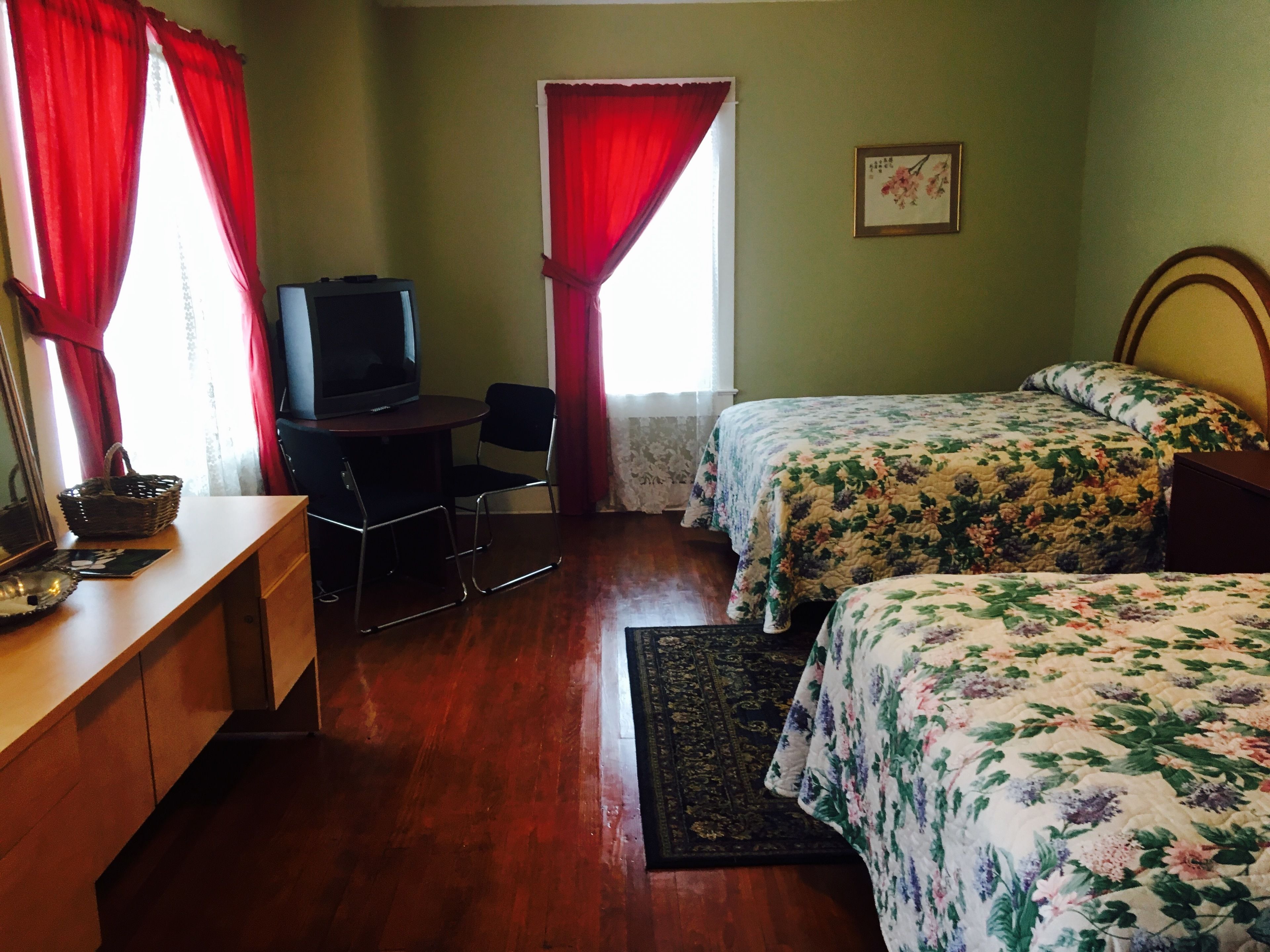A room with a bed, a desk with a chair, a television, and a window with red curtains.