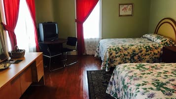 A room with a bed, a desk with a chair, a television, and a window with red curtains.