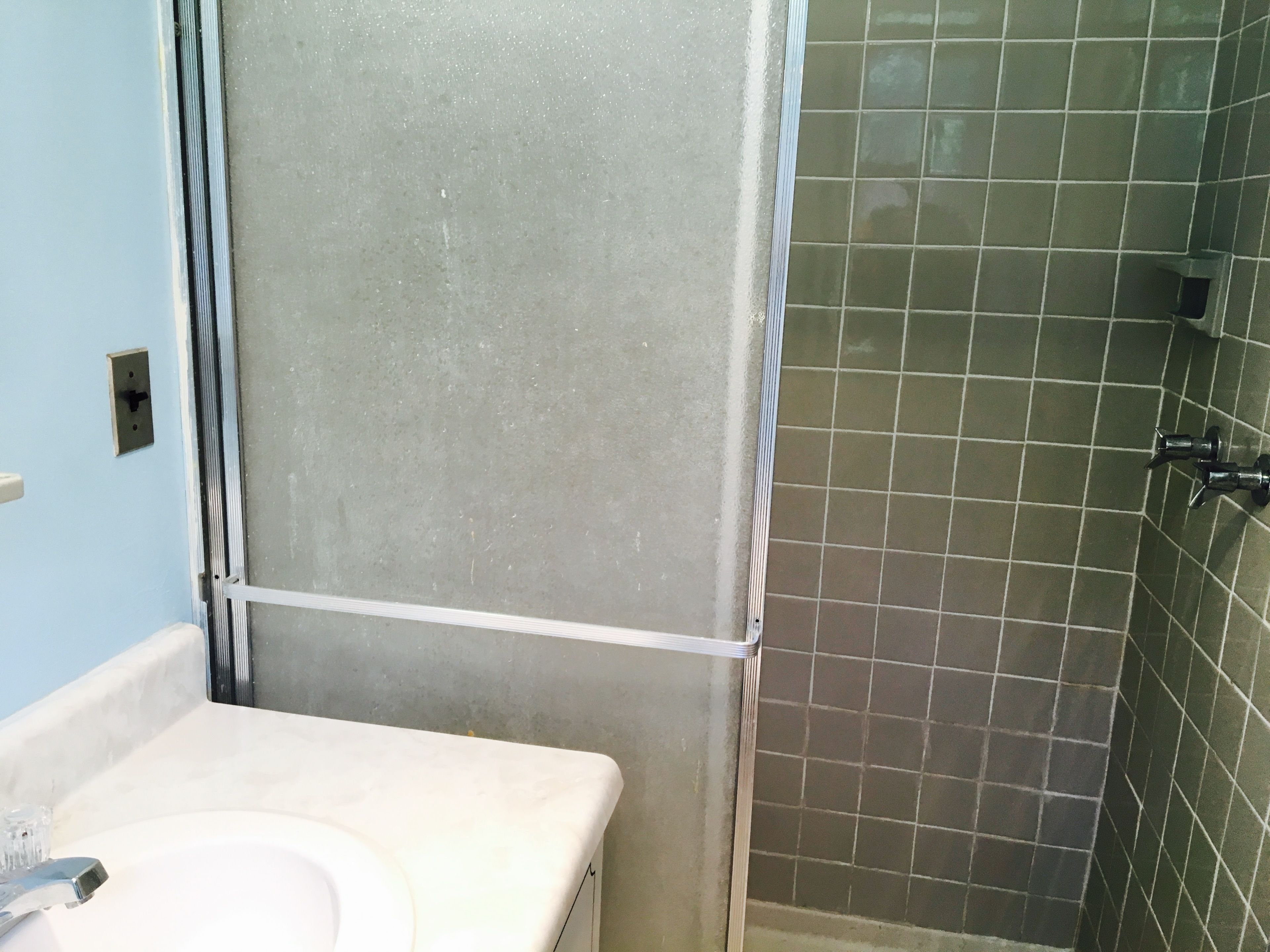 A bathroom with a white sink, a shower curtain, and green-tiled walls.